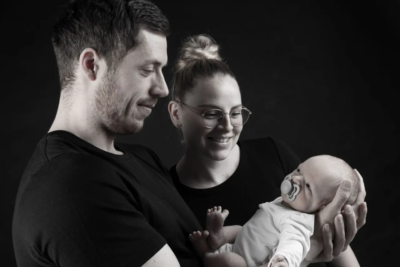 Smilende forældre holder deres lille baby i armene